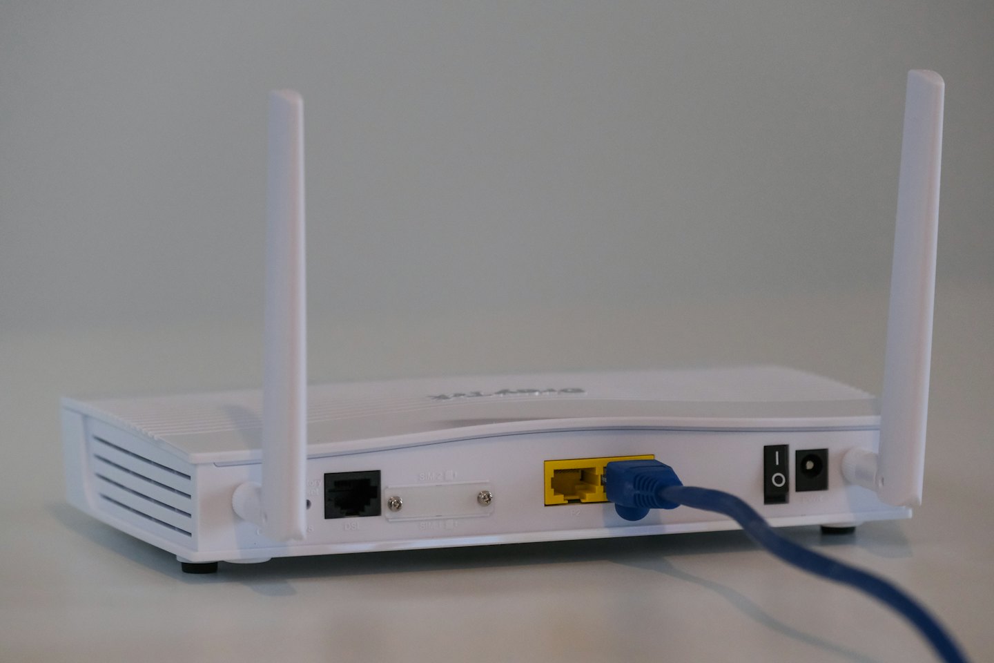 White wireless router with ports and antennas, blue ethernet cable plugged in.