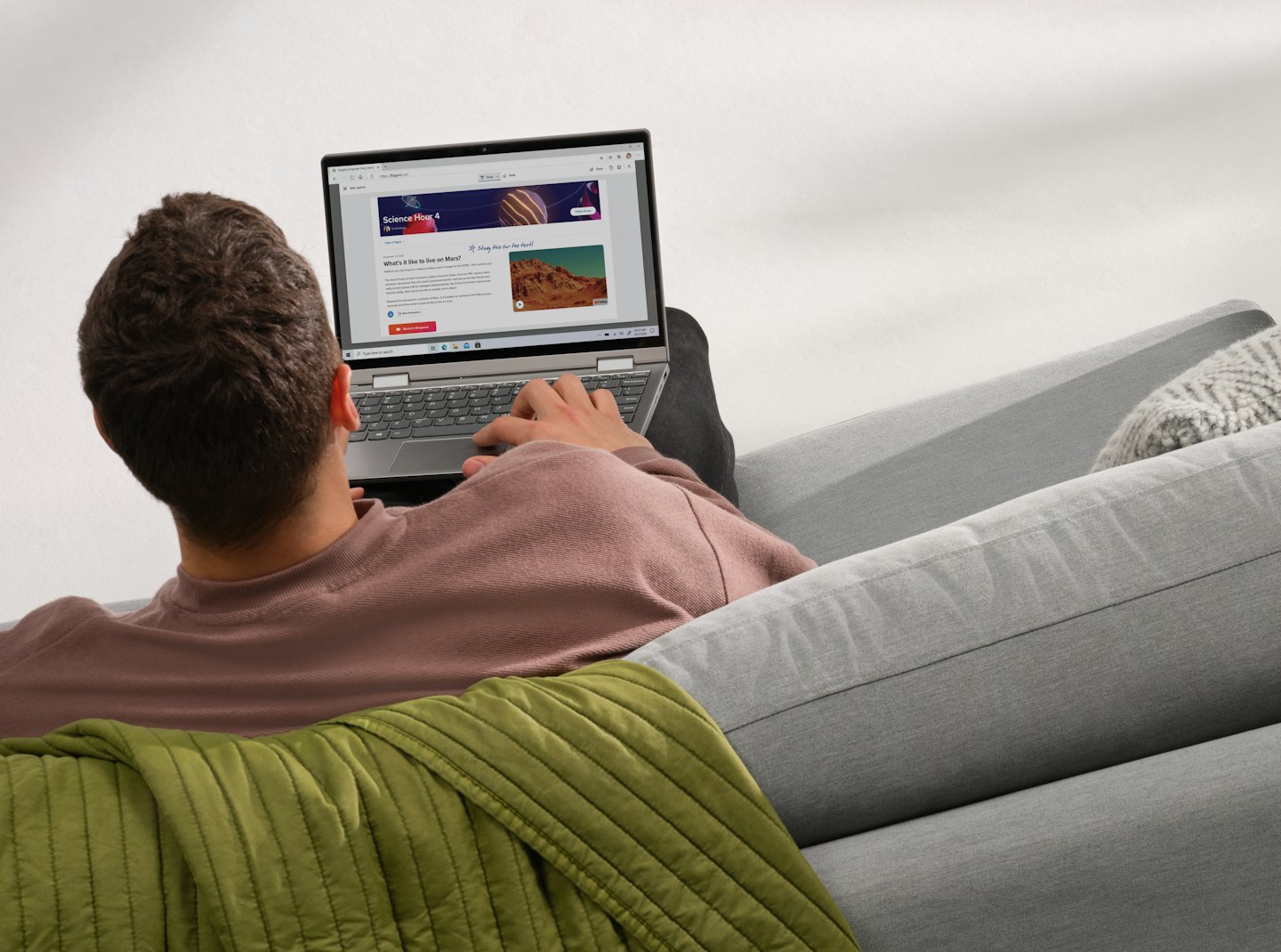 Person uses a laptop to study on a grey sofa.
